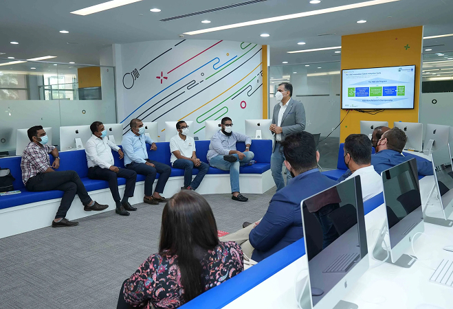 A group of people seated in a room, each using a computer, engaged in discussion or work