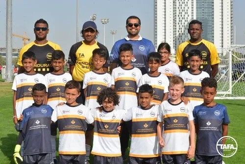 A group of young soccer players smiling and posing together for a team photo on a sunny day